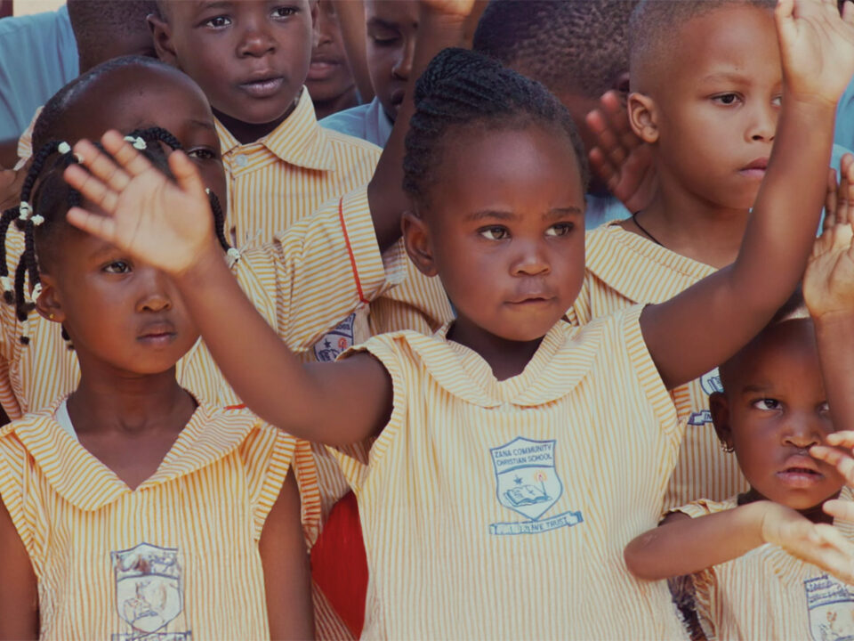 helfende hände - Eine Gruppe kleiner Kinder in einheitlichen gelb-weiß gestreiften Uniformen steht beieinander, wobei einige die Arme heben. Die Kinder scheinen an einer Schulveranstaltung oder einer Versammlung im Freien teilzunehmen. helfende hände ggmbh hamburg
